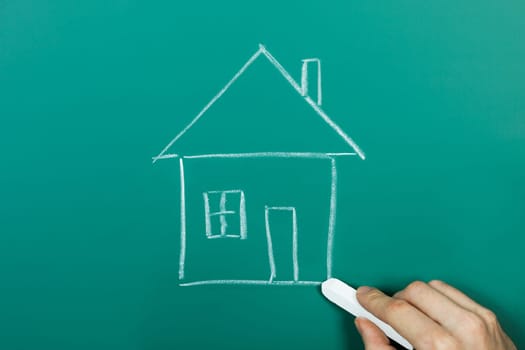 Hand holding chalk drawing house on blackboard
