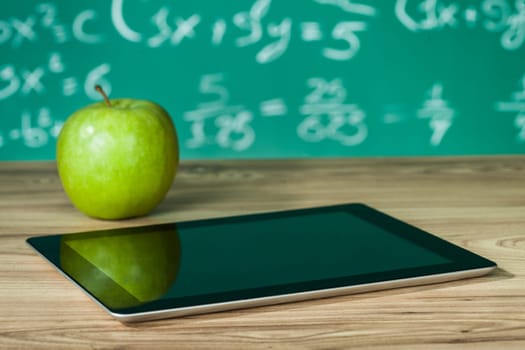 Digital tablet and apple on the desk in front of blackboard