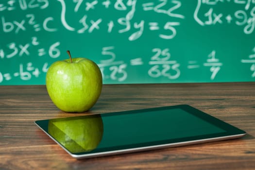 Didital tablet and apple on the desk in front of blackboard