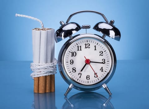 Cigarettes Tied With Rope And Alarm Clock Over Blue Background