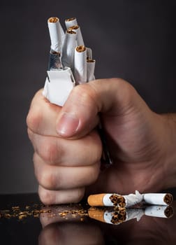 Close-up Of  Man's Fist Crushing Cigarettes Over Black Background