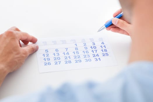 Close-up Of Man Holding Pen And Looking At Date On Calendar