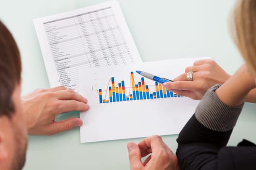 Over the shoulder view of two business partners discussing a colorful fluctuating bar graph comparing it with a text table