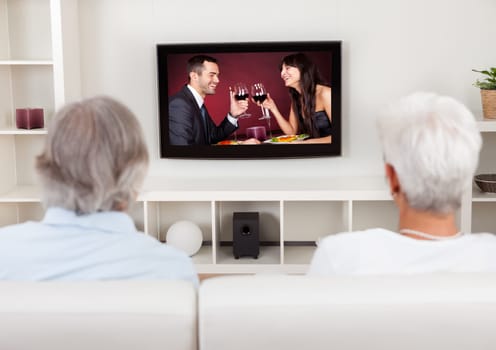 Rear view of a couple watching television with a scene on the screen of a young man and woman celebrating