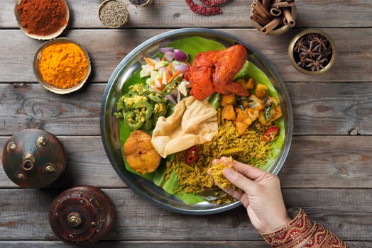 Overhead view of Indian woman's hand eating biryani rice on wooden dining table.