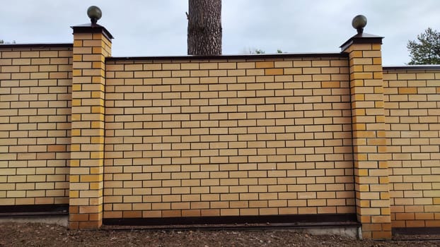 High stone modern fence made of yellow or white brick and columns with turrets. Background, texture and location