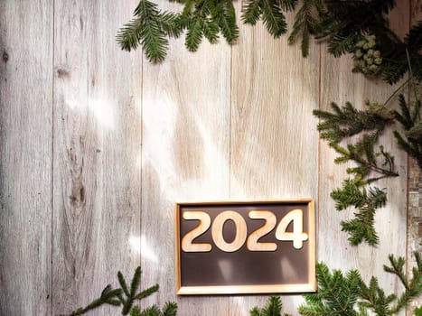 Wooden figures and numbers of the new year 2024 with frame and fir branches of Christmas tree. Celebration. Abstract background, pattern, frame, place for text, copy space