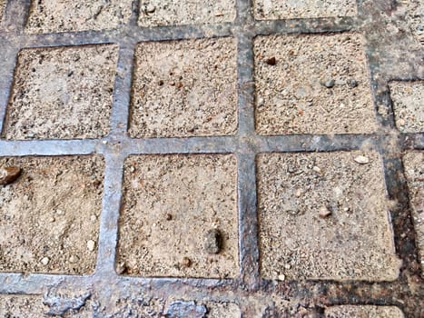 Squares in a metal grid lying on concrete, pebbles, earth. The old sidewalk or wall. Pattern of metal rods. Background, texture, frame, copy space