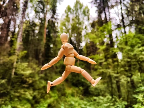 Wooden toy mannequin in forest among grass and trees in summer, autumn, spring. The concept of outdoor recreation and hiking. Healthy lifestyle. Earth Day. Save planet concept. Partial focus, blur
