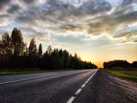 Dramatic sunset over asphalt road. Track goes into the distance in the evening summer, autumn or spring evening or night