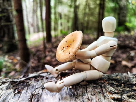 Wooden toy mannequin in a summer or autumn forest with a mushroom. The concept of mushroom picking, nature walk, autumn abundance