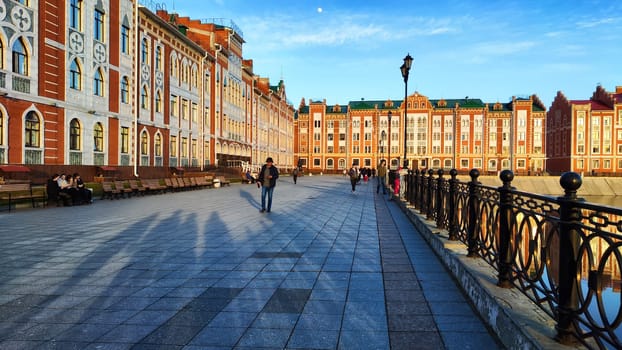 Yoshkar-Ola, Russia - April 03, 2023: The embankment of the city with houses and people in evening. The city of Yoshkar-Ola and the Bruges Embankment