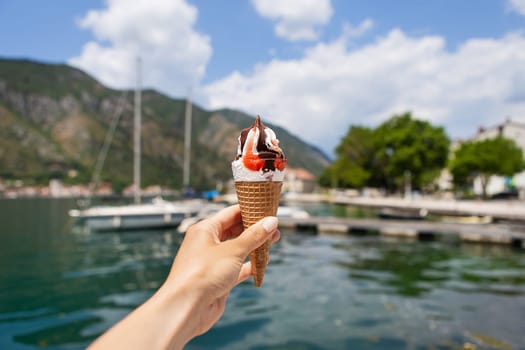 Very beautiful embankment of the Bay of Kotor, Montenegro. A girl holds colorful ice cream on the background of the Bay of Kotor