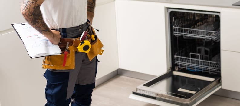 man repairing dishwasher. Male hand with screwdriver installs kitchen appliances, close up.