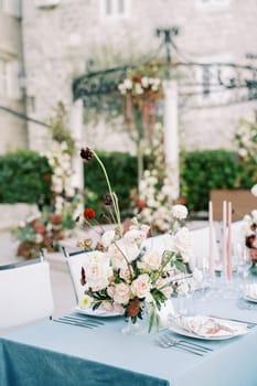 Bouquet of flowers on a festive table next to candles and plates. High quality photo