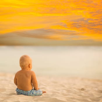 Baby sitting on the sand and looking sunset