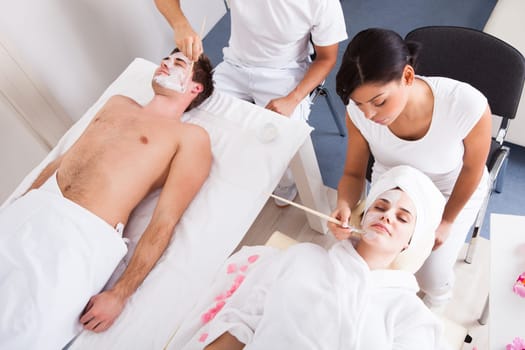 Therapist Applying Facial Mask To Young Couple At Beauty Salon