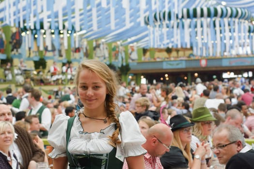 MUNICH, GERMANY – SEPT. 21, 2014: Oktoberfest Crowds of visitors at the Spatenbrau Tent celebrating the festivities with Smiling Waitress. The Festival runs from Sept. 20 – Oct. 5 in Munich, Germany