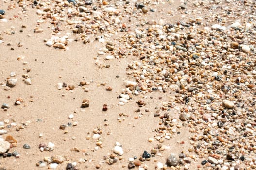 Small pebbles on sand beach closeup wetted by sea water as backgound