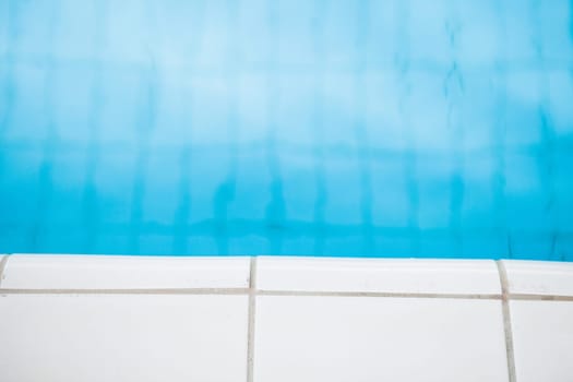 Closeup of white tiles at edge of swimming pool with blue water in background