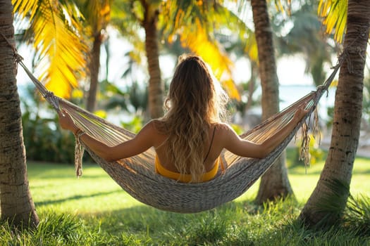 A woman enjoys a peaceful moment in a hammock, swaying gently amid palm trees on a warm, sunny day near the beach.
