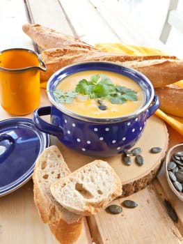 Homemade kuerbis soup in blue saucepan and fresh baguette