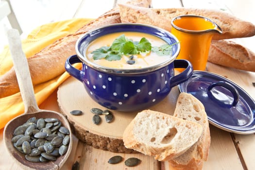 Homemade kuerbis soup in blue saucepan and fresh baguette