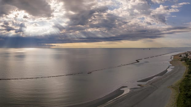 Aerial view of sandy beach and stormy sky with sun rays piercing the clouds, flat sea at dawn, Italy