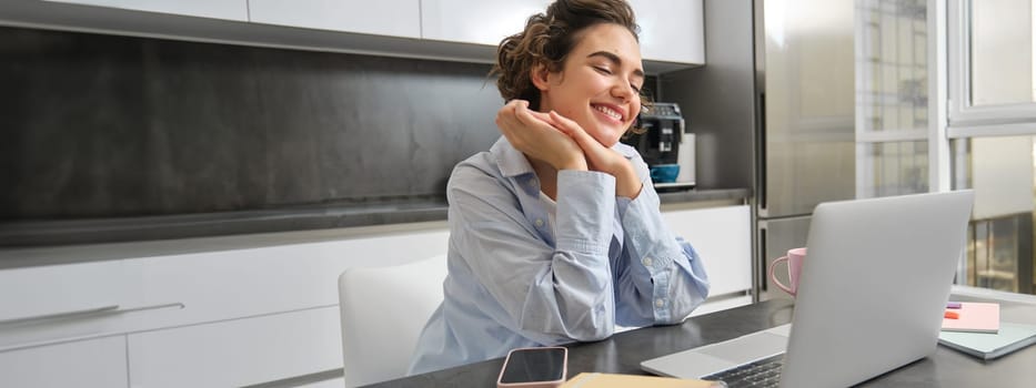 Working woman using laptop at home, doing her taxes paperwork, watching online course in kitchen.