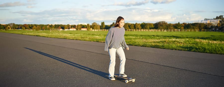 Hobbies and lifestyle. Young woman riding skateboard. Skater girl enjoying cruise on longboard on sunny day outdoors.