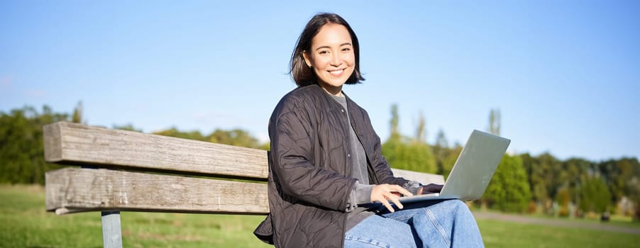 Digital nomad. Portrait of young woman using laptop in park, sitting on bench and working, studying online.