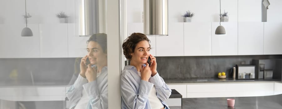 Portrait of cute young woman answers a phone call, talks on smartphone, spends time at home. Copy space