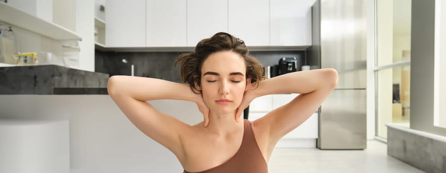 Home sports and wellbeing. Young brunette woman in sportswear, staying at home and doing yoga, mindful exercises, sitting in yoga pose with eyes closed and relaxed face. Copy space