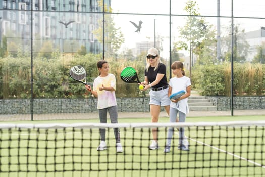 Young tennis trainer in activewear holding racket held by one of two cute girls while consulting her during individual training on stadium. High quality photo