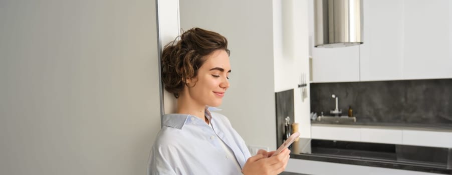 Portrait of brunette woman with smartphone, sending message, checking her mobile application, ordering delivery to home.