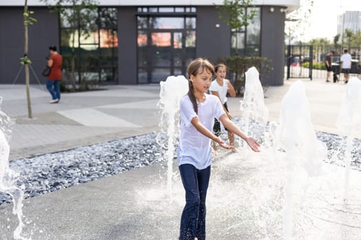 Happy teenage girl dancing in a fountain in a city park on a hot summer day. High quality photo
