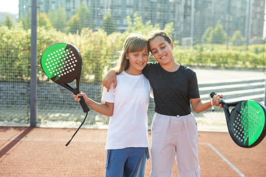 Teenage girls with racquets and balls standing in padel court, looking at camera and smiling. High quality photo