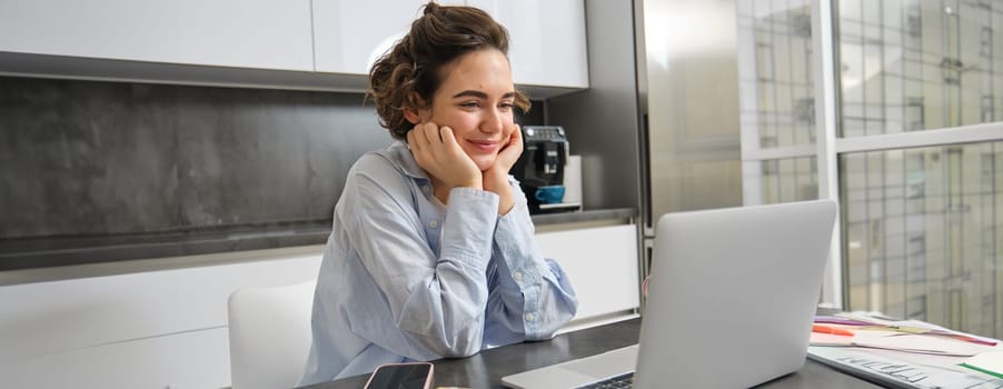 Image of smiling woman studying on remote, looking at laptop while sitting at home, watching webinar, doing online course on computer.