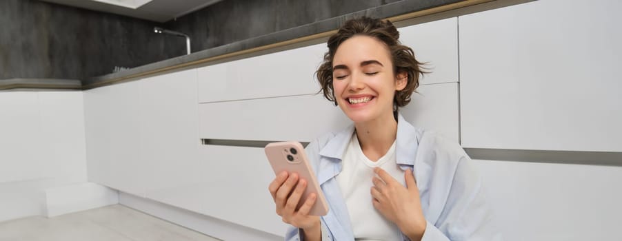 Upbeat young woman talking on mobile phone, video chats and laughs, points at herself, uses smartphone app.