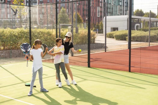 Cheerful coach teaching child to play tennis while both standing on tennis court. High quality photo