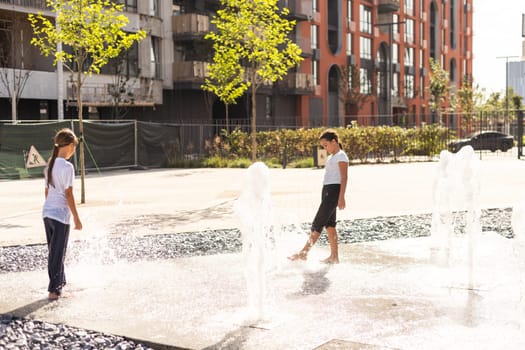 Cheerful young teen girl in city fountain, girl in wet clothes is having fun and enjoying the cool summer water, background city architecture. High quality photo