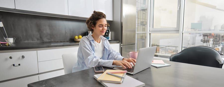 Portrait of hardworking woman studying from home, typing on laptop keyboard and smiling, working on remote, completing tax forms, managing her household bills on computer.