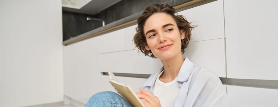 Creative young woman, writes makes notes, sits on floor at home, puts her thoughts on paper, does homework. People, lifestyle and hobbies concept