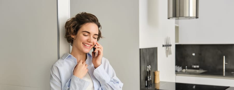 Portrait of woman talking on mobile phone and smiling, spending time at home, has telephone conversation, answers a call.