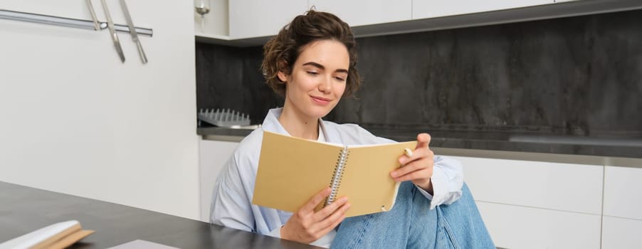 Image of brunette girl reading through her notes, writing in journal, studying while sitting at home.