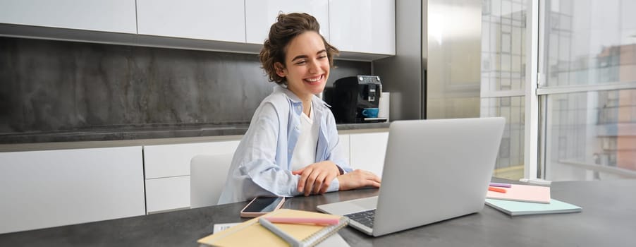 Portrait of smiling young woman connects to online webinar, studies at home on remote, looking at laptop with happy face, teacher people via tutor website.