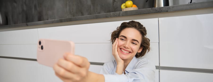 Portrait of happy, beautiful woman takes selfie on smartphone, extends her hand with mobile phone and takes picture of herself, records vlog on mobile phone.