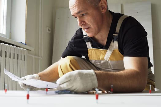 A male worker studies instructions before assembling furniture. Overall plan.