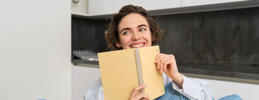 Happy young woman studying at home, reading journal, preparing for exam, looking at her notes in notebook. Copy space