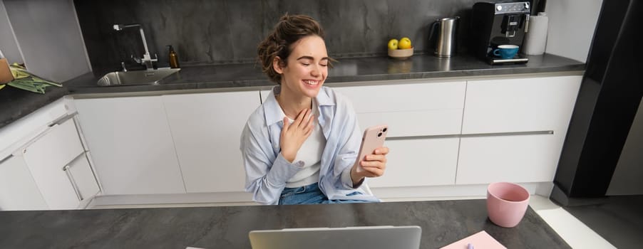 Portrait of candid young woman, laughing, using laptop and smartphone, video chats, joing online conversation, team meeting from home.
